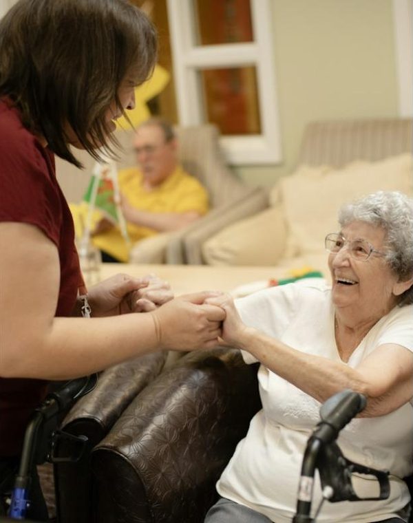 A caregiver holding the hands of a smiling older woman