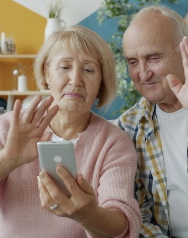 An older couple waving at a phone on a video call